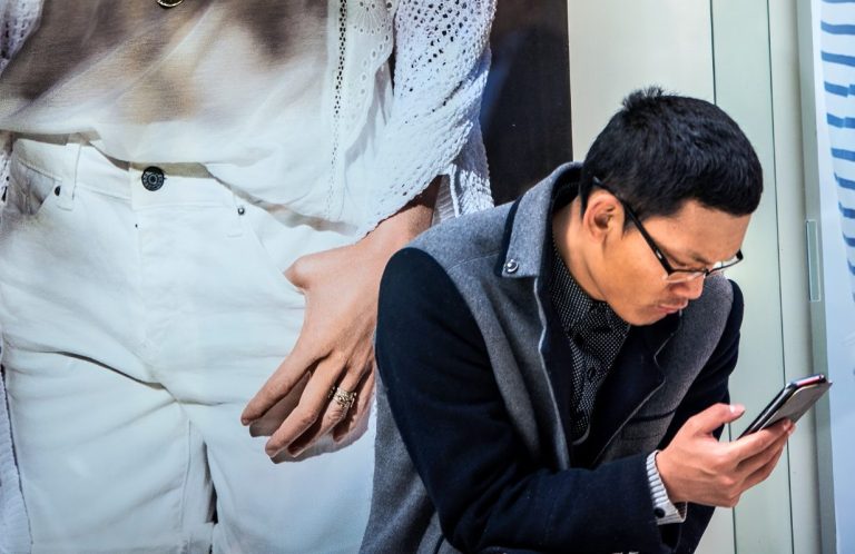 Geplante Bildwelt für einen Markenauftritt Mann mit Smartphone vor einer großformatigen Markeninszenierung im urbanen Umfeld.